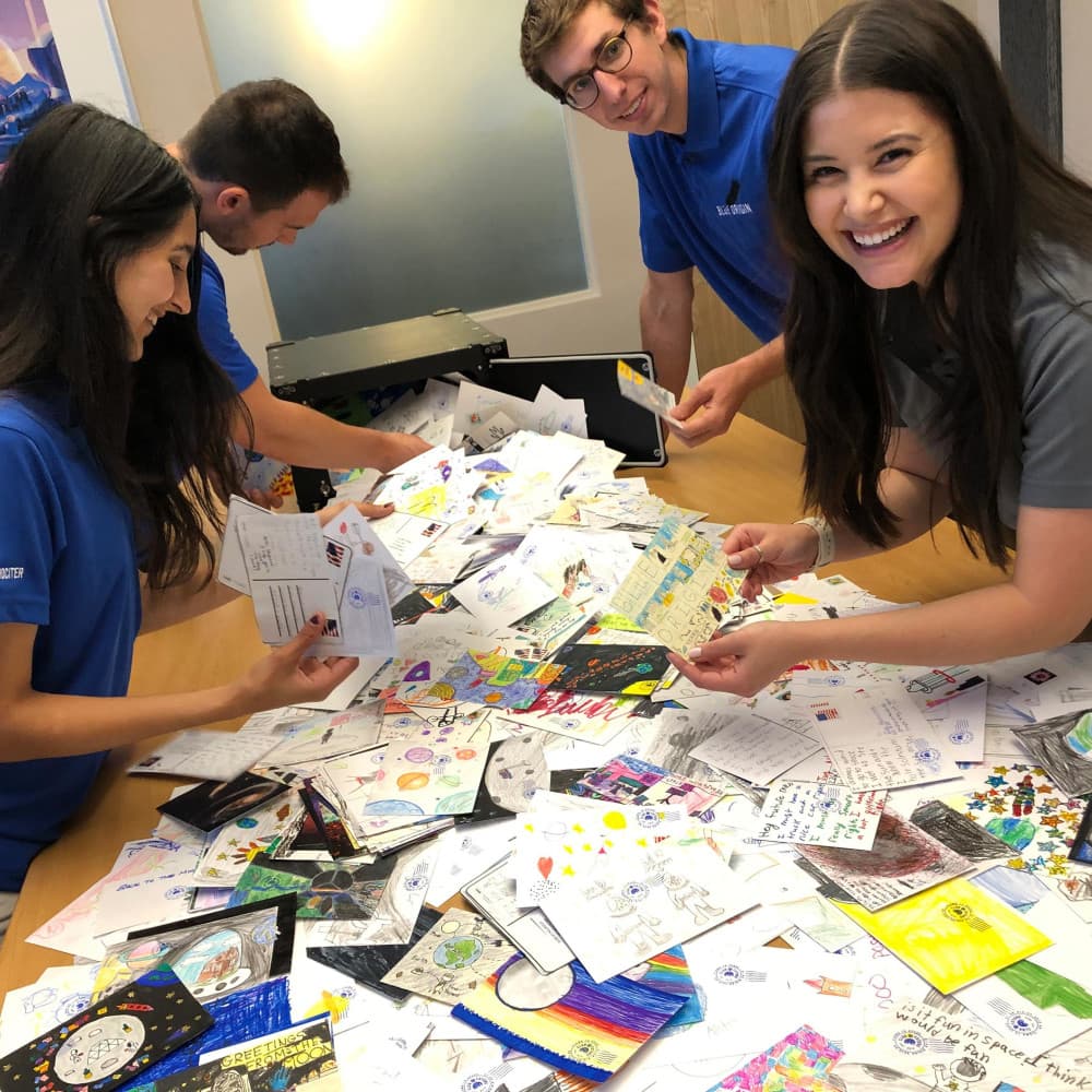 Four people stand around a table covered in illustrated postcards