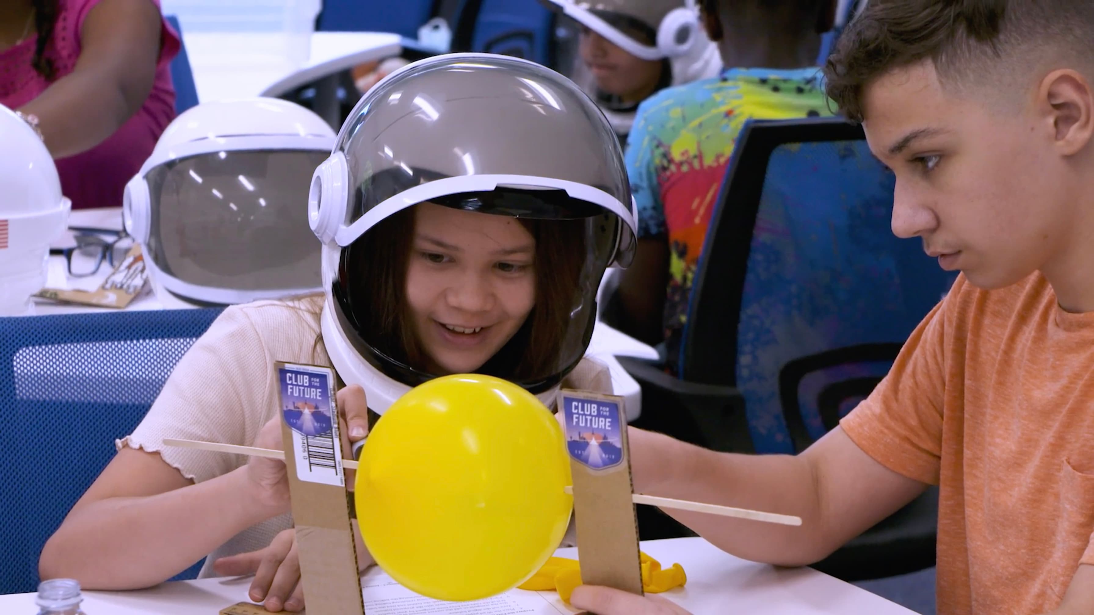 Two kids focus on an science experiment with a yellow balloon