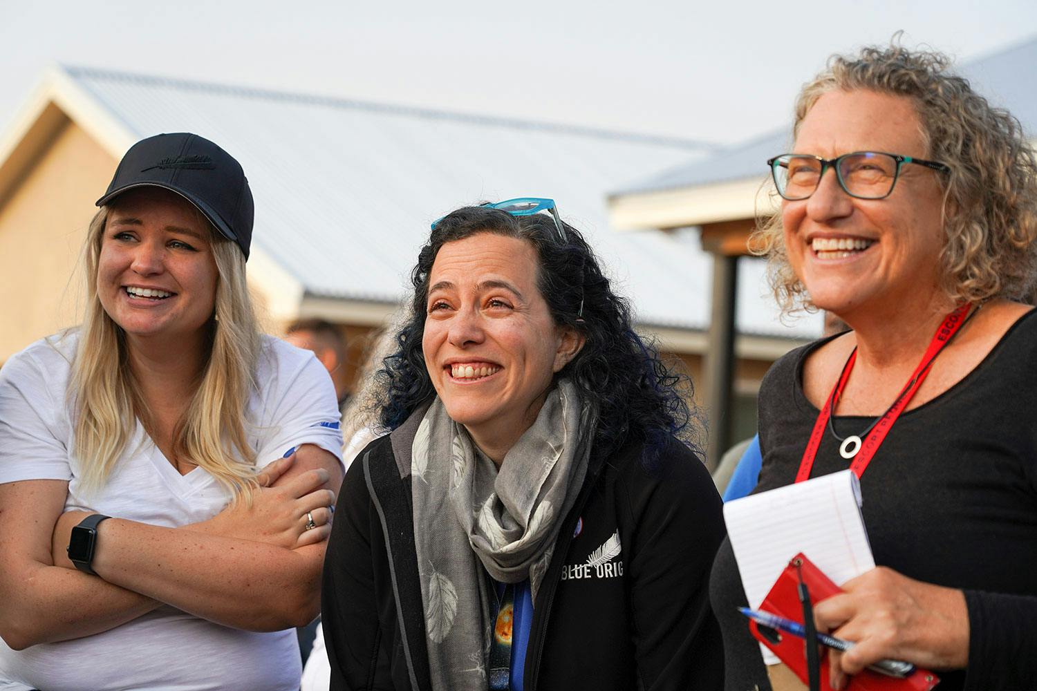 Three smiling women look off into the distance during a launch weekend, Erika Wagner in the center