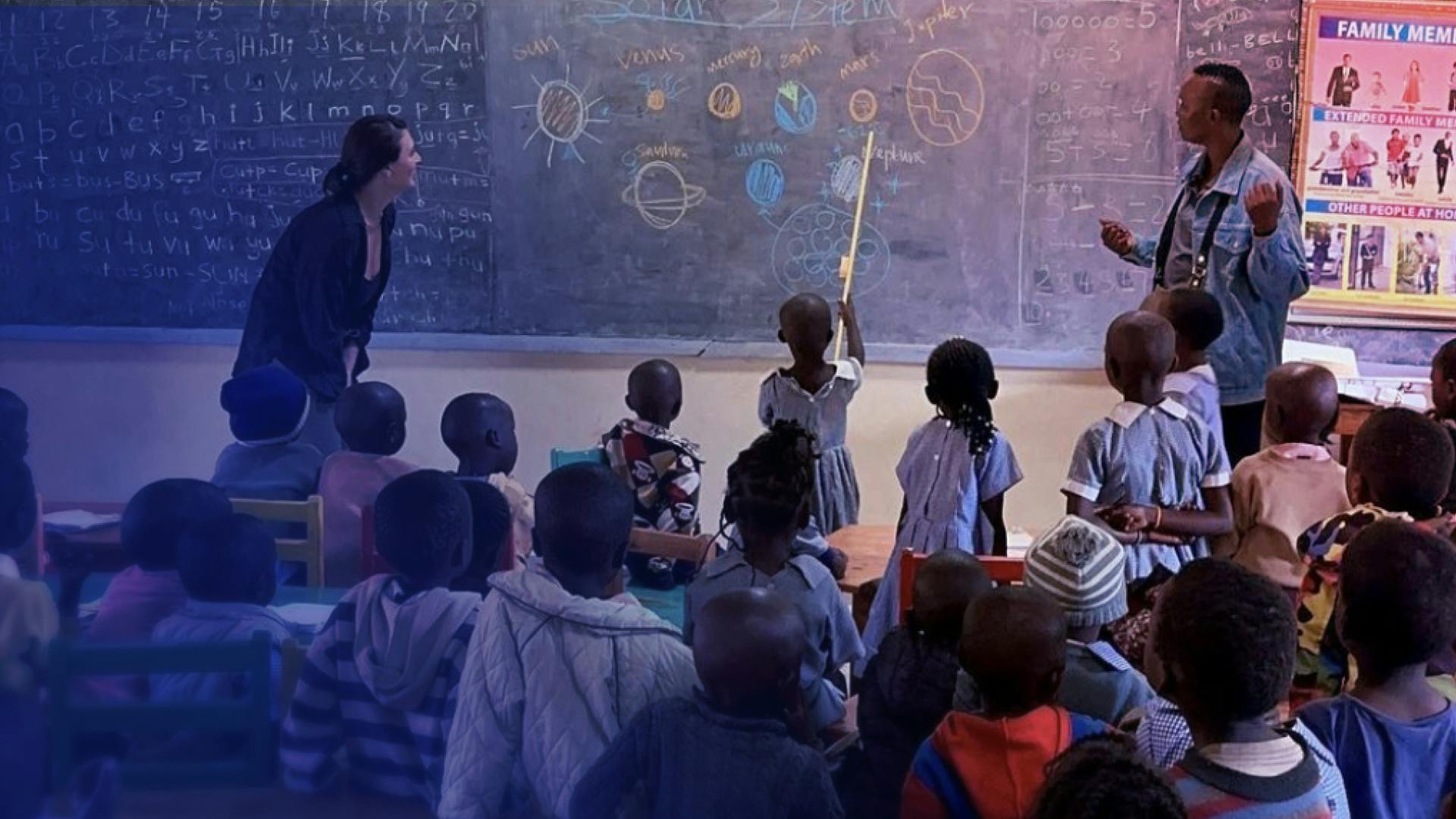 Students in a classroom in Africa are looking to the front of the room where the solar system is drawn on a chalkboard