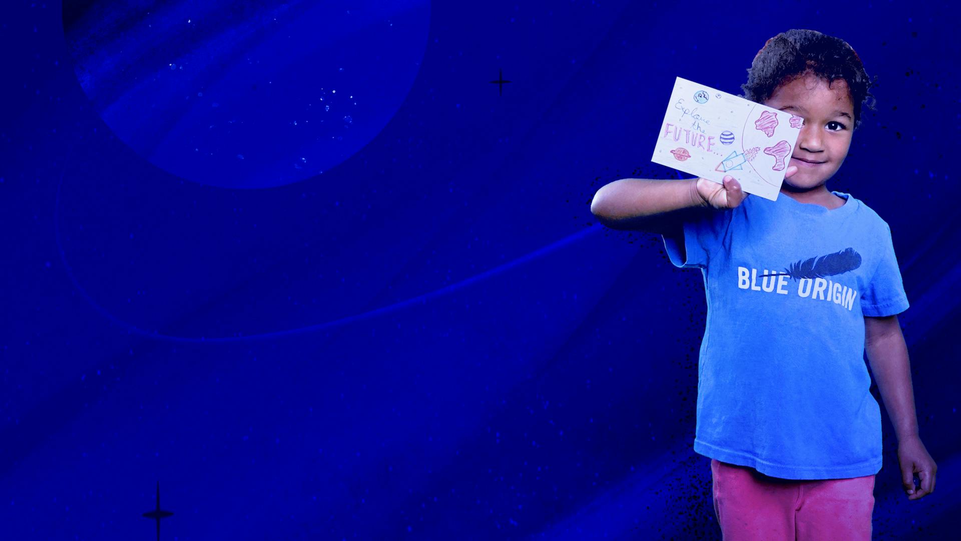 A young girl in a Blue Origin T-shirt holds up a paper postcard covered in drawings.