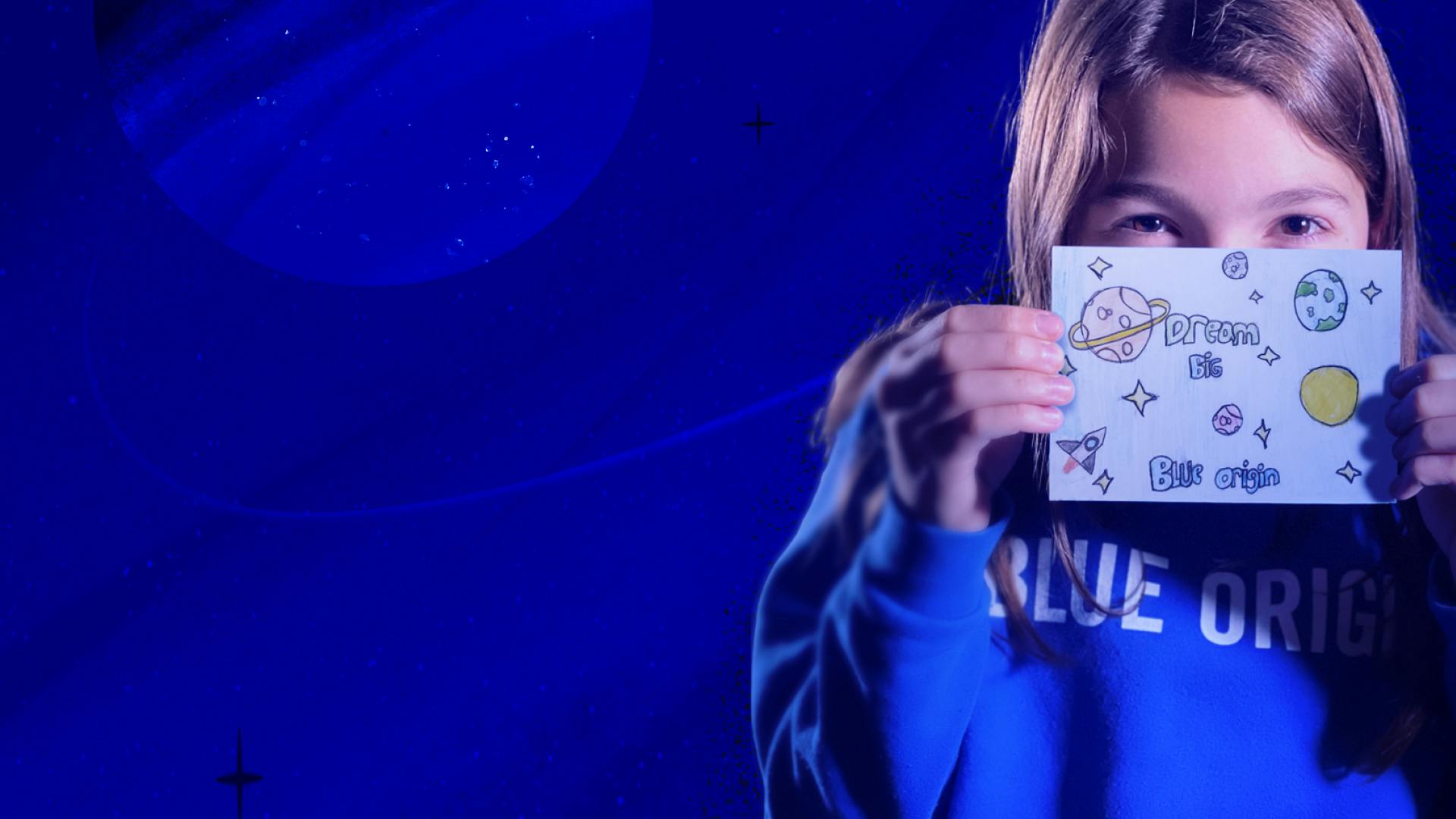 A girl in a 'Blue Origin' sweatshirt holds a paper postcard up to her face