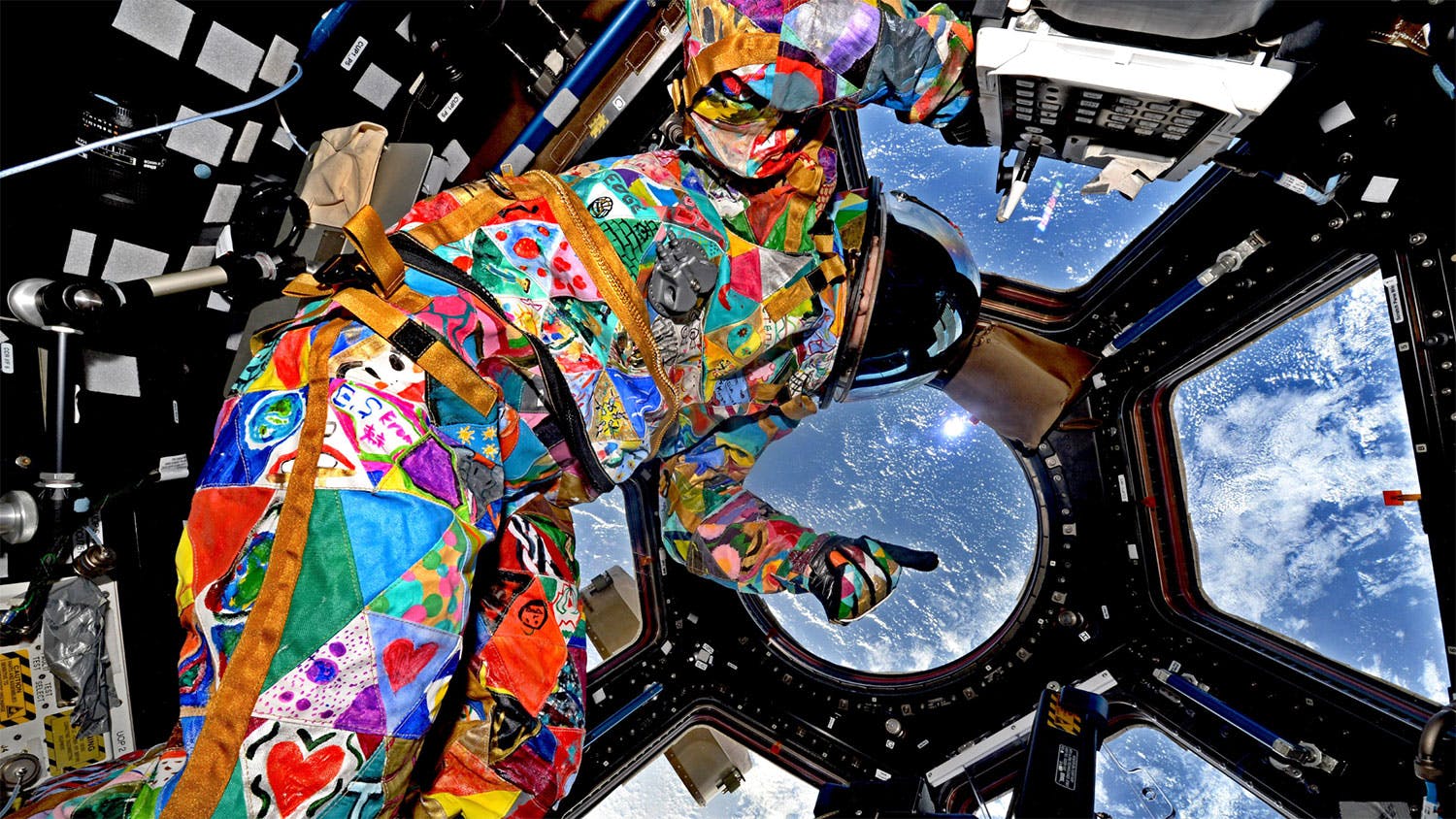 An astronaut wearing a vibrant, colorful spacesuit floats in a capsule