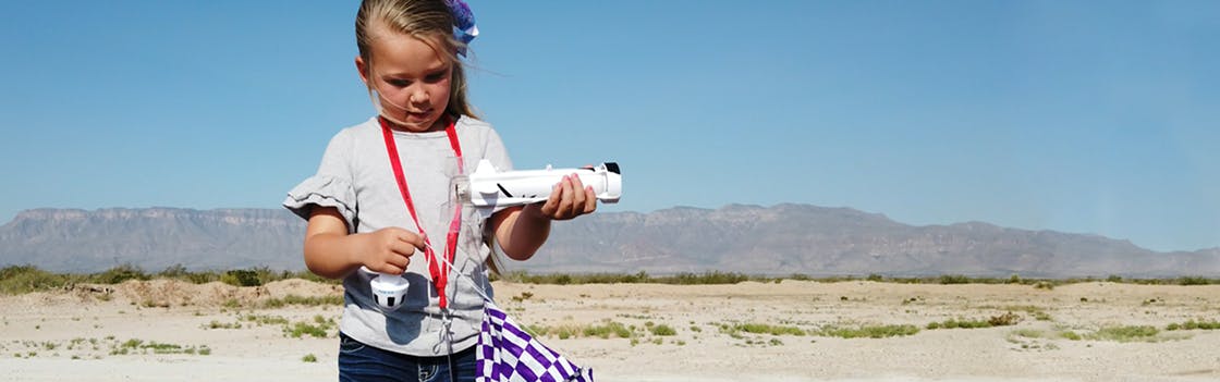 A young girl holds a New Shepard model rocket