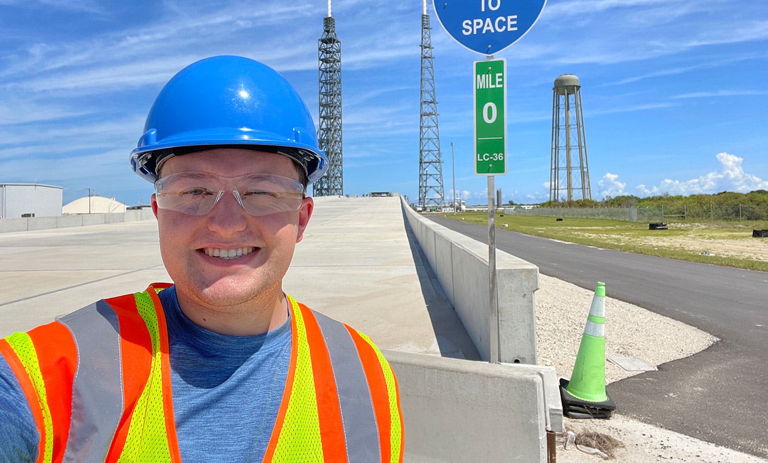 A person in a blue construction hat and safety vest stands in front of the New Glenn launch pad