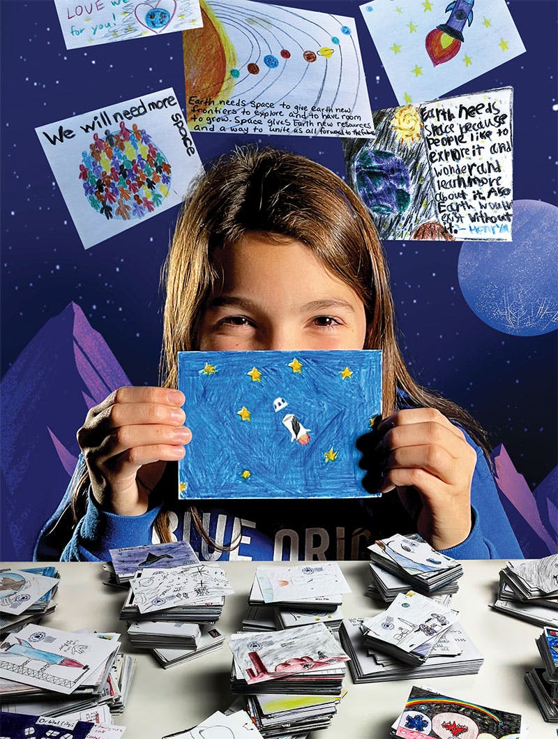 A girl holds up a drawing on a postcard to her nose, surrounded by other sample postcards that will be sent to space